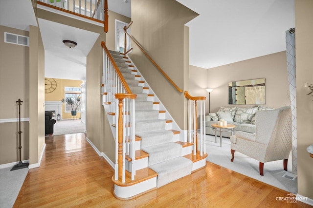 staircase with a fireplace, wood finished floors, visible vents, and baseboards