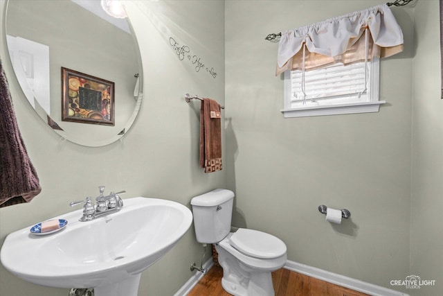 half bathroom featuring wood finished floors, toilet, baseboards, and a sink