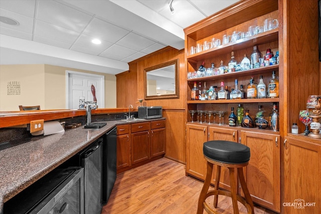 bar featuring wet bar, a sink, black dishwasher, light wood-style floors, and stainless steel microwave