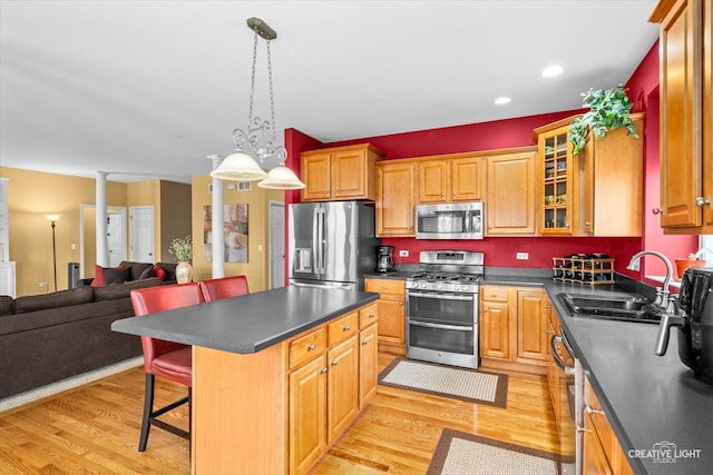 kitchen with light wood-style flooring, a sink, stainless steel appliances, dark countertops, and a kitchen breakfast bar