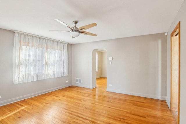 unfurnished room with arched walkways, ceiling fan, visible vents, baseboards, and light wood-style floors