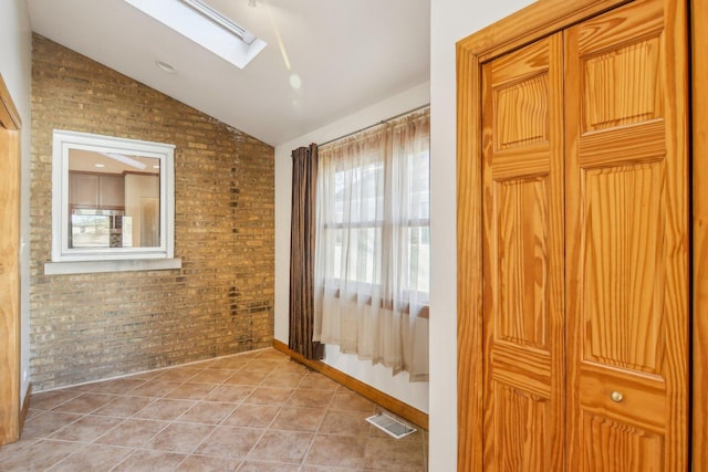 doorway to outside featuring vaulted ceiling with skylight, light tile patterned flooring, visible vents, and brick wall