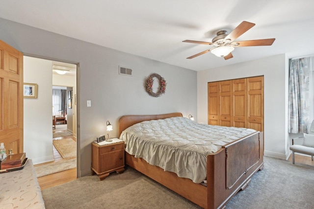 bedroom with a closet, light colored carpet, visible vents, a ceiling fan, and baseboards