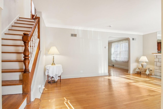 interior space with arched walkways, light wood-style flooring, stairway, and visible vents