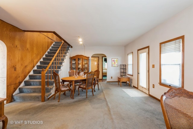 dining room featuring arched walkways, stairway, carpet flooring, and baseboards