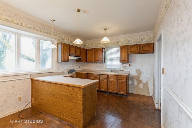 kitchen with a sink, a peninsula, brown cabinets, and wallpapered walls