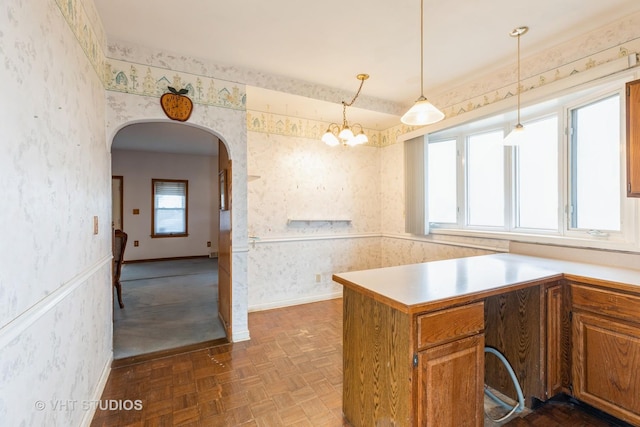 kitchen with arched walkways, baseboards, brown cabinets, and wallpapered walls