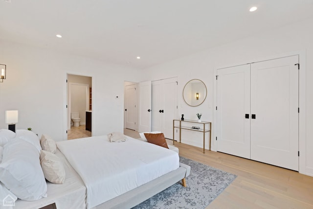 bedroom with ensuite bath, light hardwood / wood-style flooring, and multiple closets