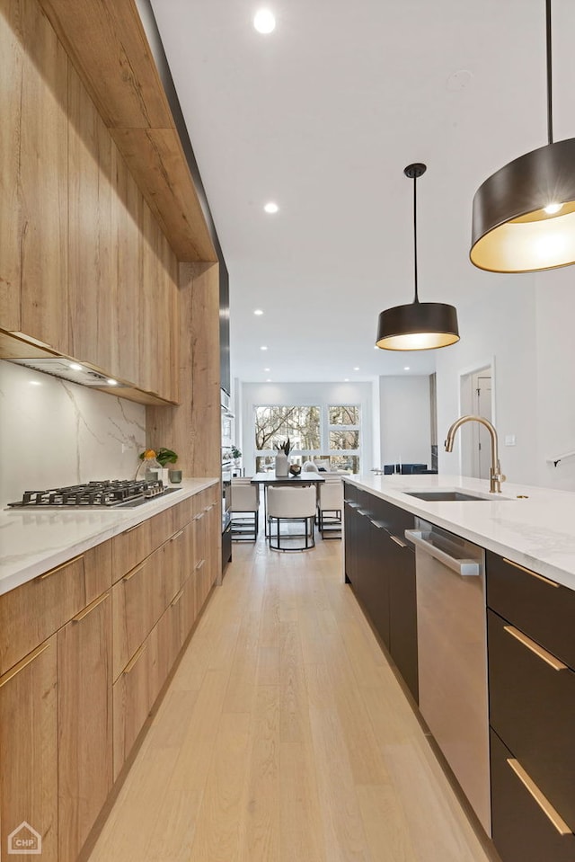 kitchen featuring light stone countertops, light hardwood / wood-style floors, sink, appliances with stainless steel finishes, and pendant lighting