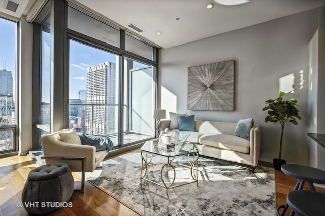 living room with a view of city, visible vents, expansive windows, and wood finished floors