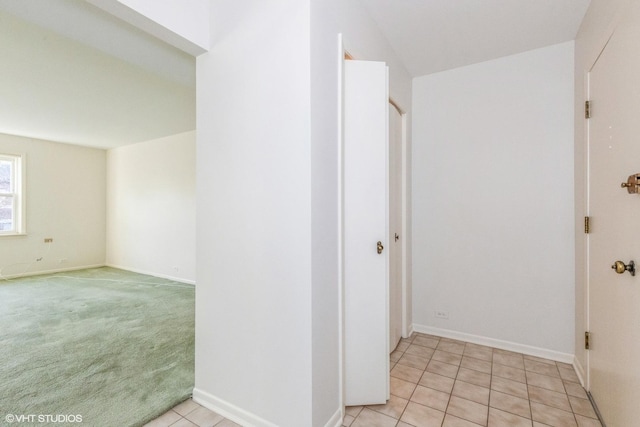 hall with light carpet, light tile patterned floors, and baseboards