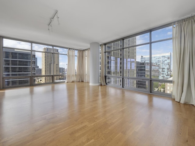 spare room with expansive windows, a city view, track lighting, and wood finished floors