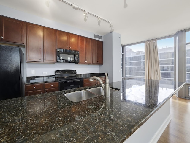 kitchen featuring a sink, visible vents, light wood-type flooring, dark stone counters, and black appliances