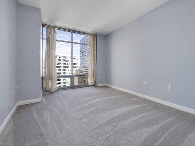 unfurnished room with a view of city, a wall of windows, carpet flooring, and baseboards