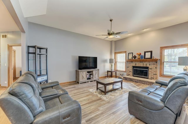 living area with ceiling fan, light wood finished floors, a brick fireplace, and baseboards