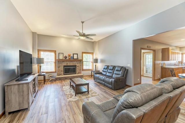 living area with a ceiling fan, baseboards, a fireplace, and light wood finished floors