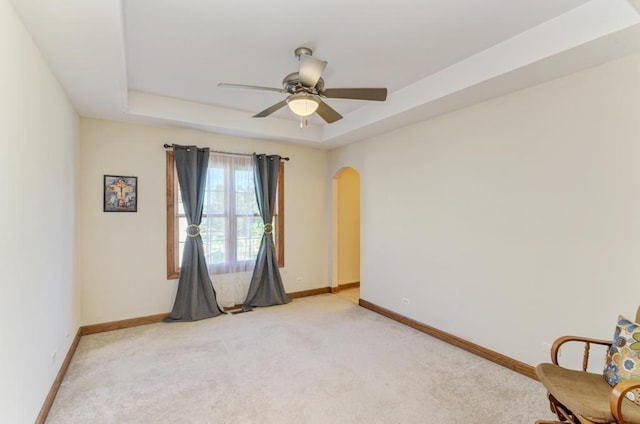 unfurnished room with arched walkways, a raised ceiling, light colored carpet, and baseboards