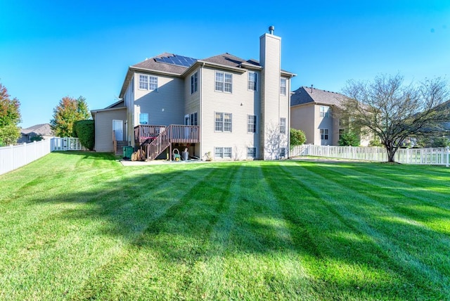 rear view of house featuring a chimney, a lawn, stairway, roof mounted solar panels, and a fenced backyard