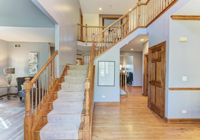 stairway with recessed lighting, wood finished floors, a towering ceiling, visible vents, and baseboards