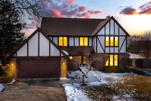 english style home with stucco siding, driveway, a shingled roof, brick siding, and a chimney