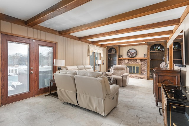 living room featuring built in shelves, beam ceiling, french doors, wood walls, and a brick fireplace