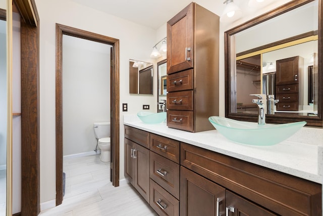 bathroom featuring double vanity, toilet, baseboards, and a sink