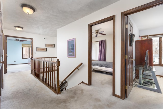 hall featuring an upstairs landing, baseboards, a textured ceiling, and carpet