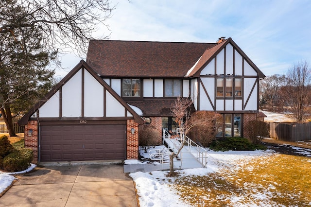 tudor home featuring stucco siding, brick siding, a garage, and driveway