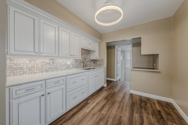 kitchen featuring dark wood-type flooring, light stone counters, white cabinets, decorative backsplash, and sink