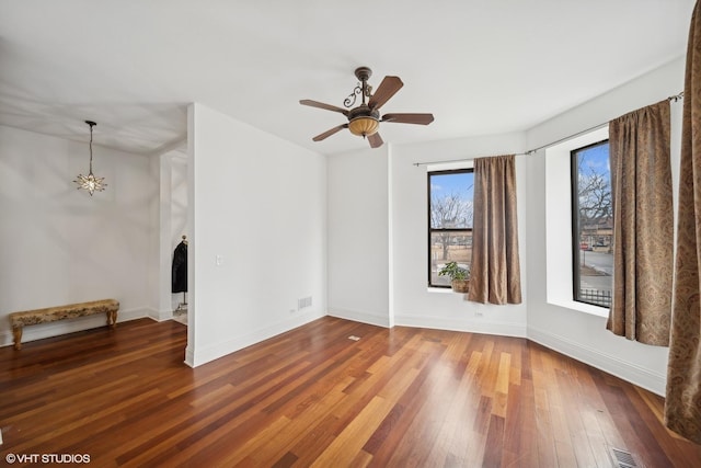 empty room featuring visible vents, baseboards, wood finished floors, and ceiling fan with notable chandelier