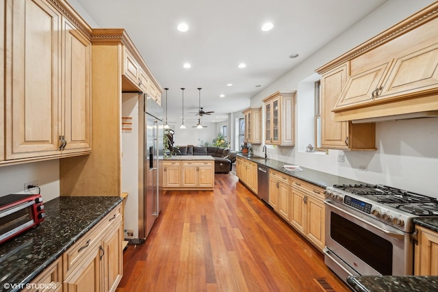 kitchen with appliances with stainless steel finishes, dark stone counters, light brown cabinets, and hanging light fixtures