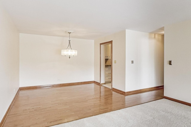 empty room with a chandelier, baseboards, and wood finished floors