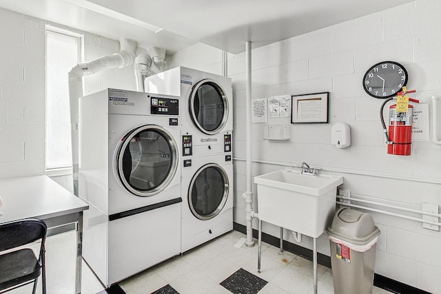 community laundry room with concrete block wall, stacked washing maching and dryer, a sink, and washer and dryer