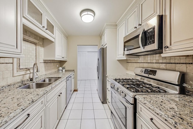 kitchen with light stone counters, light tile patterned flooring, stainless steel appliances, a sink, and backsplash