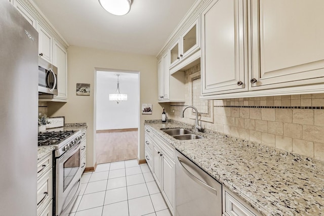 kitchen featuring stainless steel appliances, tasteful backsplash, light tile patterned flooring, a sink, and light stone countertops