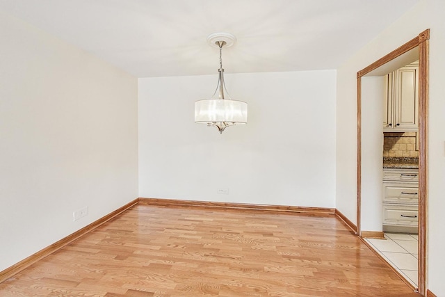 unfurnished dining area featuring light wood-style floors, a chandelier, and baseboards