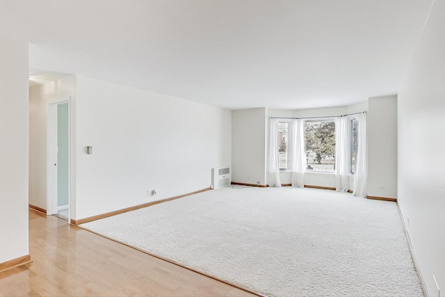 empty room with heating unit, light colored carpet, light wood finished floors, and baseboards