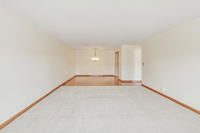 empty room with a chandelier, light colored carpet, and baseboards