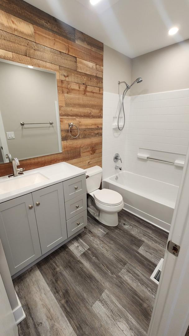 full bathroom featuring toilet, vanity, wooden walls, and wood-type flooring