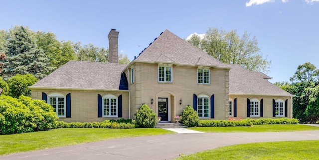 view of front of home with a front lawn, brick siding, roof with shingles, and a chimney