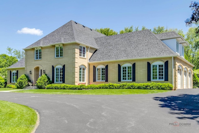 view of front of house featuring aphalt driveway, a garage, brick siding, and roof with shingles