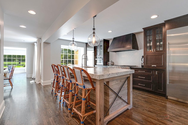 kitchen with dark wood-style floors, a sink, stainless steel appliances, wall chimney range hood, and backsplash