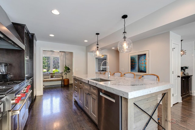 kitchen with wall chimney range hood, dark wood finished floors, a kitchen bar, appliances with stainless steel finishes, and a sink