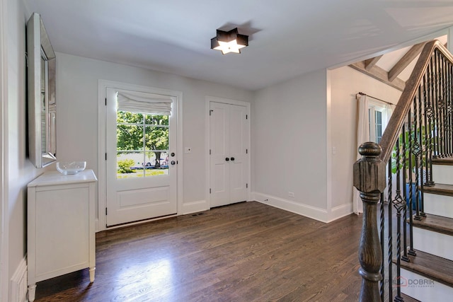 foyer entrance with dark wood finished floors, stairs, and baseboards