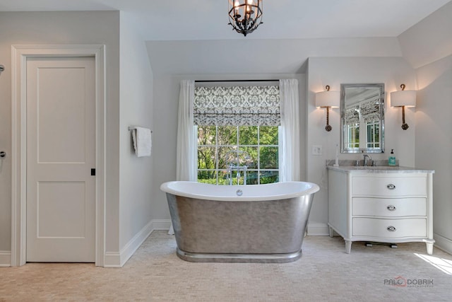 full bathroom with vanity, a freestanding tub, a notable chandelier, and baseboards