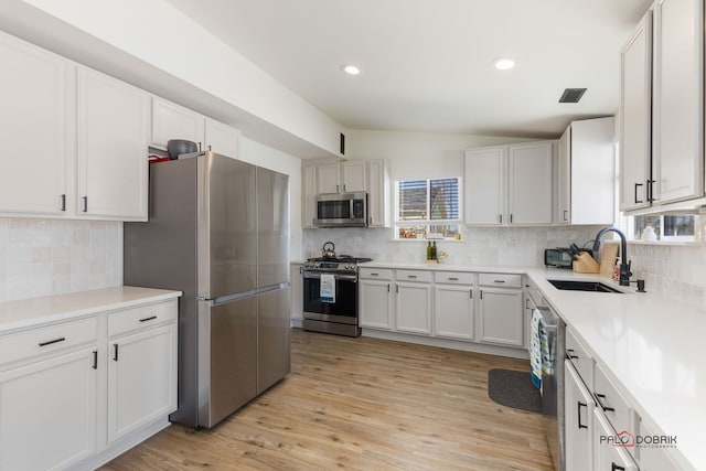 kitchen with white cabinets, lofted ceiling, appliances with stainless steel finishes, light countertops, and a sink