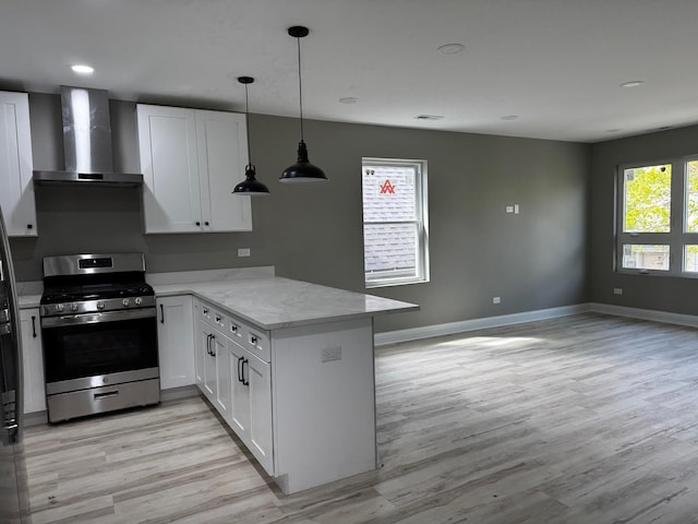 kitchen featuring stainless steel gas range, light wood-style floors, wall chimney exhaust hood, a peninsula, and white cabinets