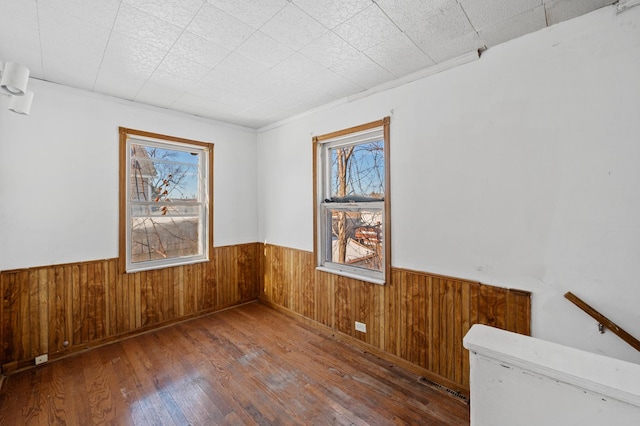 spare room featuring wooden walls, visible vents, wood finished floors, and wainscoting