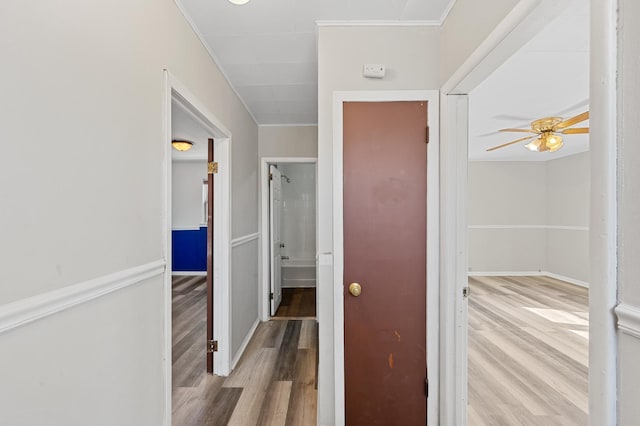 corridor with ornamental molding, light wood finished floors, and baseboards