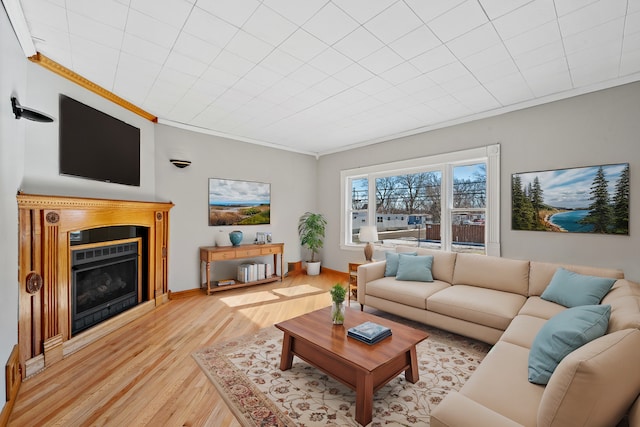 living room featuring ornamental molding, a fireplace, light wood-style flooring, and baseboards